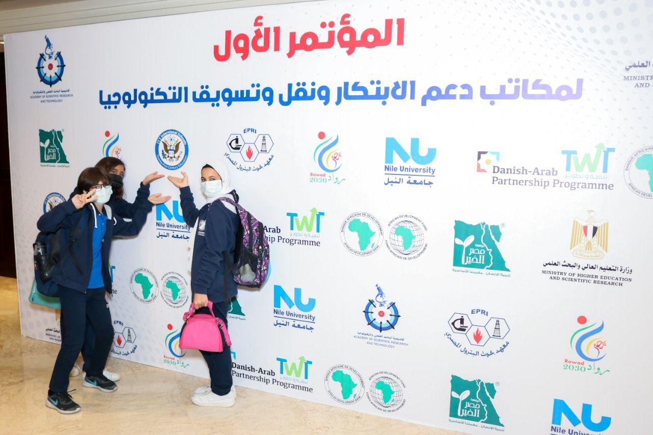 This image showcases three individuals at the IVY STEM International School Future Forum event. They are wearing face masks and casual attire, posing for a photo in front of a backdrop adorned with logos from various organizations, including Nile University and the Danish-Arab Partnership Programme. The Ministry of Higher Education and Scientific Research logo indicates the academic and educational context of the event.